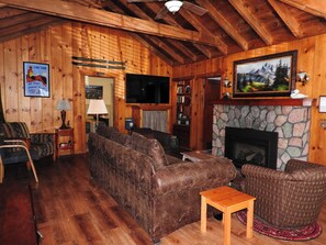 Acogedor interior de cabaña de madera con chimenea, paredes de madera, televisor y estantería.