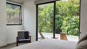 A bedroom with a large bed, a ceiling fan, a window, and a view of greenery outside.