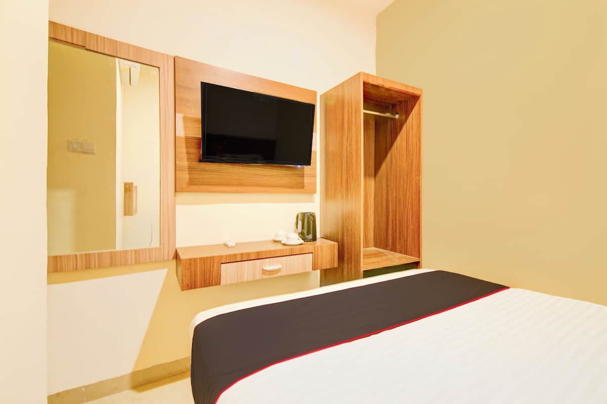 A hotel room with a bed, a television mounted on a wooden panel, a mirror, and a wooden wardrobe.