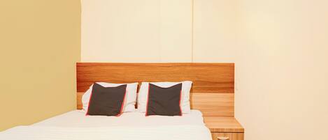 A neatly made bed with a wooden headboard, two pillows, and a small bedside table with a drawer.