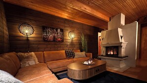 A cozy living room with a wooden ceiling, a sectional sofa, a round coffee table, and a fireplace. - Nesset Fiskfjord. House by the sea with panoramic views, Gateway to Lofoten! (Troms)