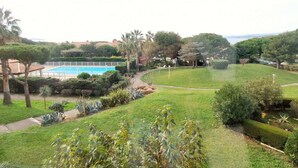 A landscaped garden with a swimming pool, palm trees, and a view of the sea. - Swimming pool, air conditioning, 200 m from beaches, ideal for family holidays (SIX FOURS LES PLAGES)