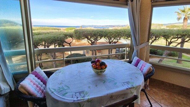 A balcony with a table set for two, a bowl of fruit, and a view of the sea and trees. - Swimming pool, air conditioning, 200 m from beaches, ideal for family holidays (SIX FOURS LES PLAGES)