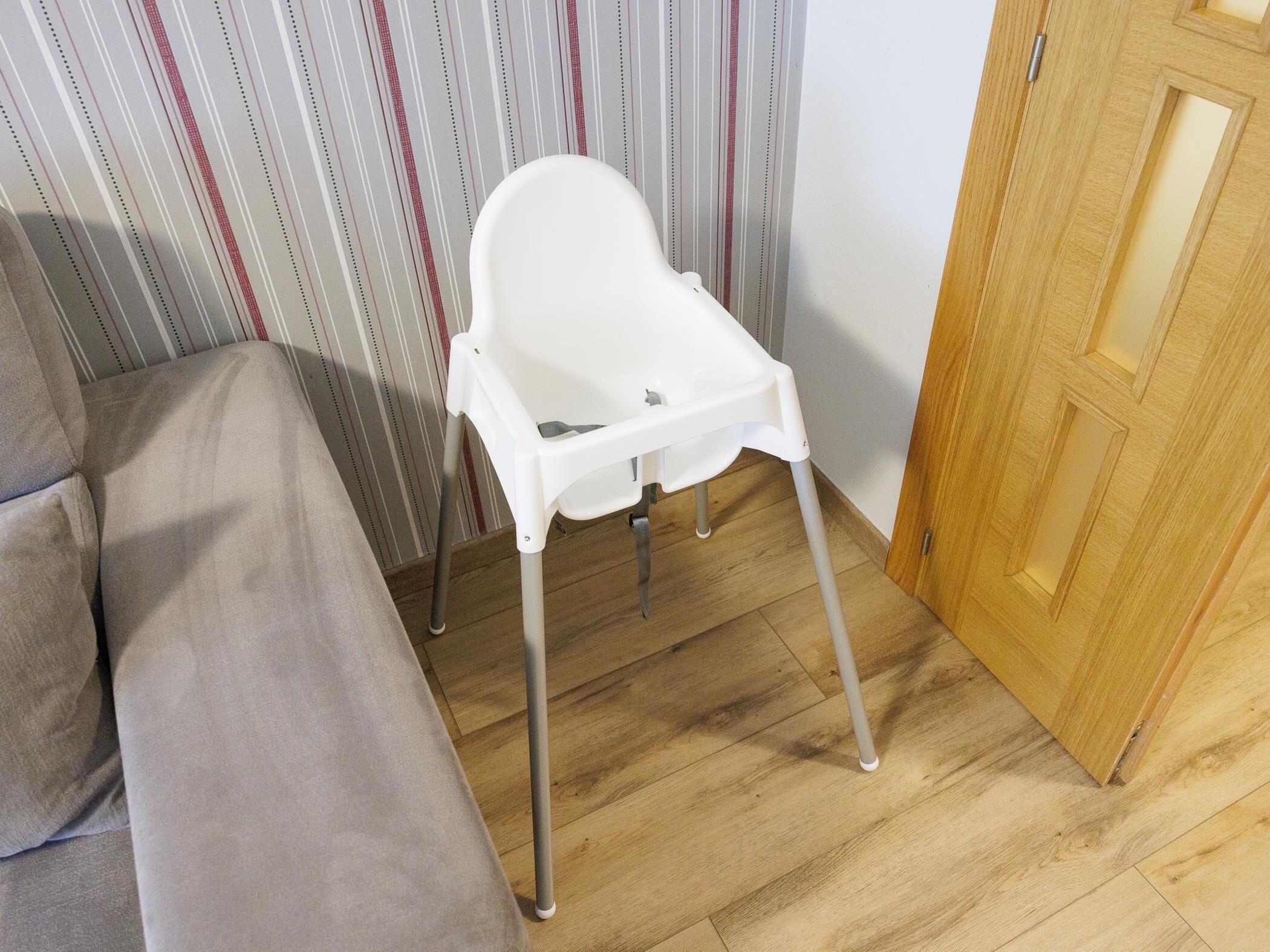 Una silla alta blanca con patas metálicas en una habitación con papel tapiz a rayas y una puerta de madera.