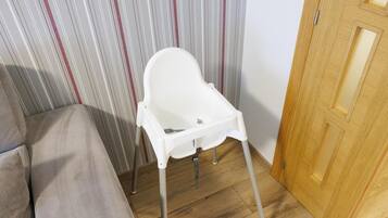 Una silla alta blanca con patas metálicas en una habitación con papel tapiz a rayas y una puerta de madera.
