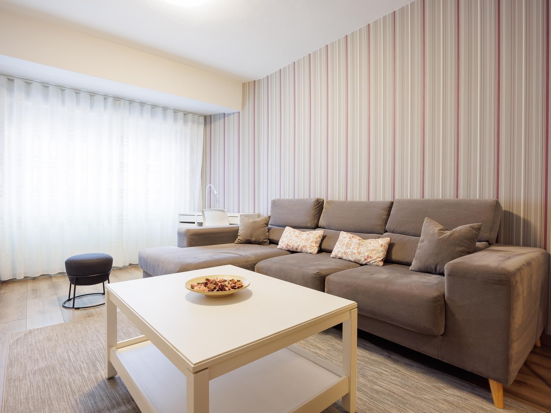 Ein modernes Wohnzimmer mit einer Couch, einem kleinen Tisch mit einer Schale und einer gestreiften Wand.