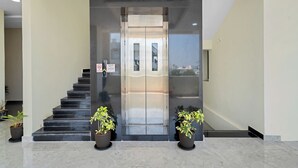 Un ascensor modern amb porta de vidre, una escala amb graons negres i plantes en test a la base.