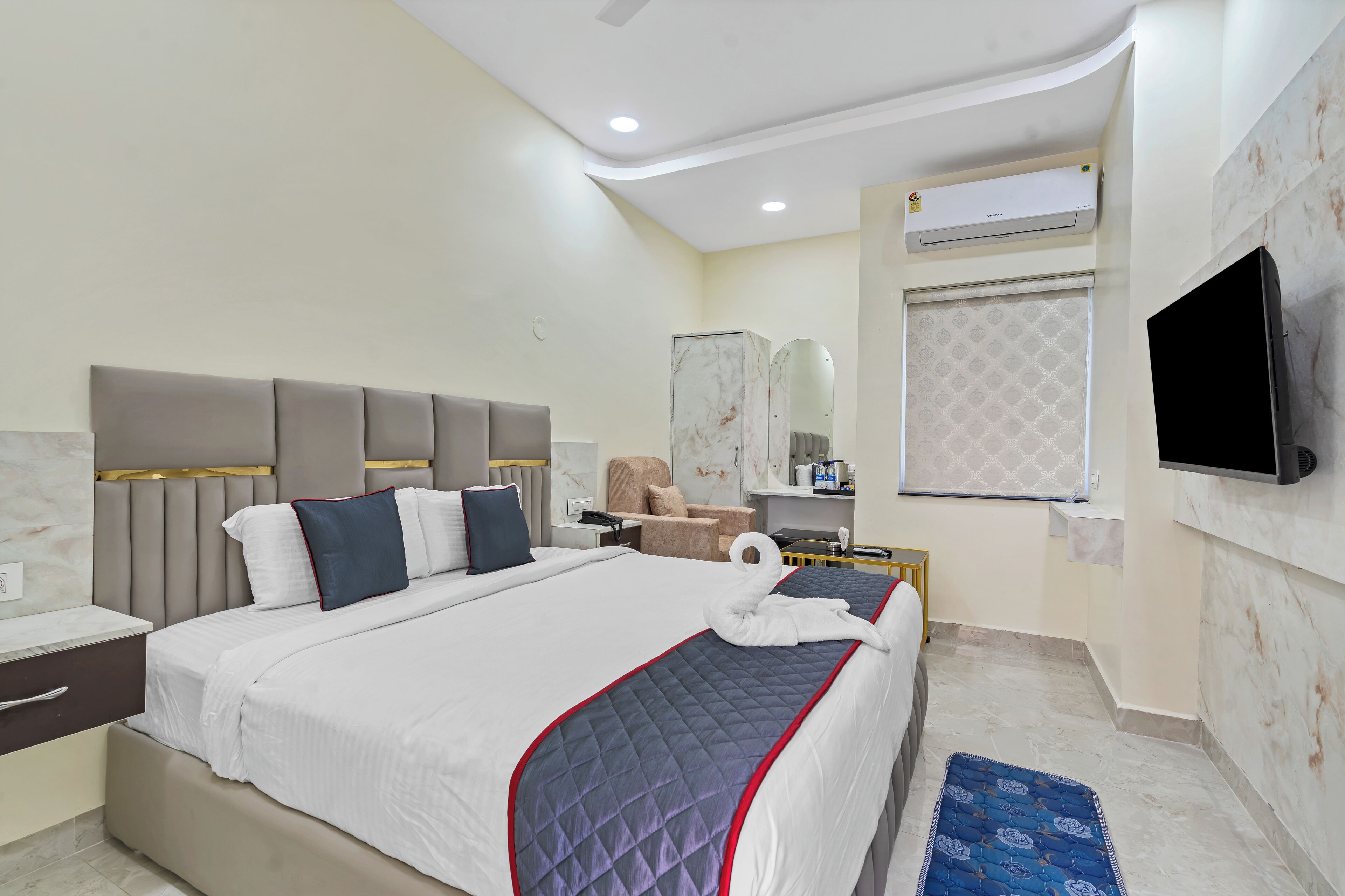 A modern hotel room with a large bed, a flat-screen TV, a vanity with a mirror, and a small seating area.