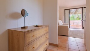 Habitación con cómoda de madera, una mesita con un plato y una silla. Se ve una puerta que da a un espacio exterior con una mesa y sillas.