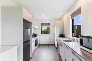 A modern kitchen with white cabinetry, stainless steel appliances, and a window providing a view of greenery outside. - AKL A/Port 6 km, free car park, spacious & Bright (Auckland)