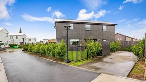 Un immeuble résidentiel moderne à deux étages, doté d’une façade sombre, d’une allée pavée et d’une pelouse bien entretenue.