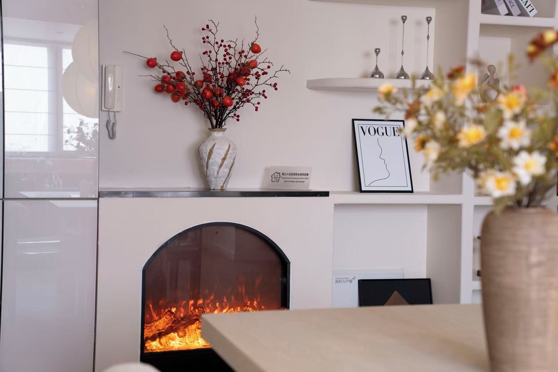 A modern interior with a fireplace, a vase with red berries, and a framed picture on the wall.