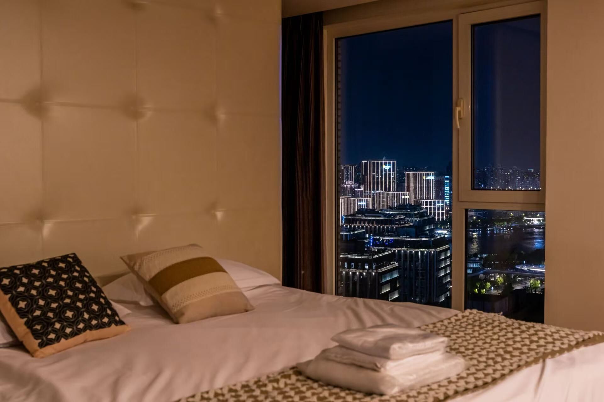 Een hotelkamer met een groot bed, uitzicht op een stadsbeeld 's nachts en een raam met gordijnen.