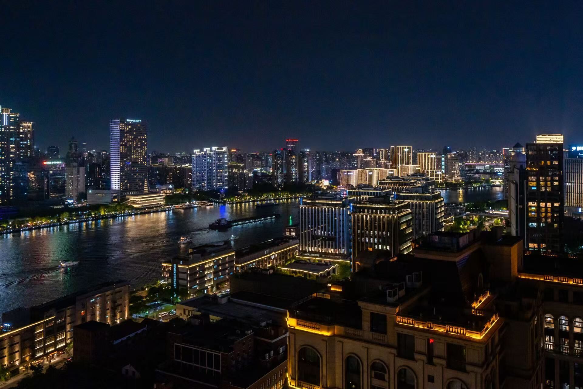 Une vue nocturne d’une ville, avec une rivière, des immeubles de grande hauteur et un hôtel imposant dont l’enseigne est illuminée.