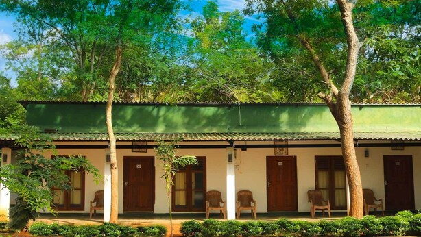 A building with a green roof and multiple doors, surrounded by trees and greenery. - Leon Lakeside Hotel (Sella Kataragama)
