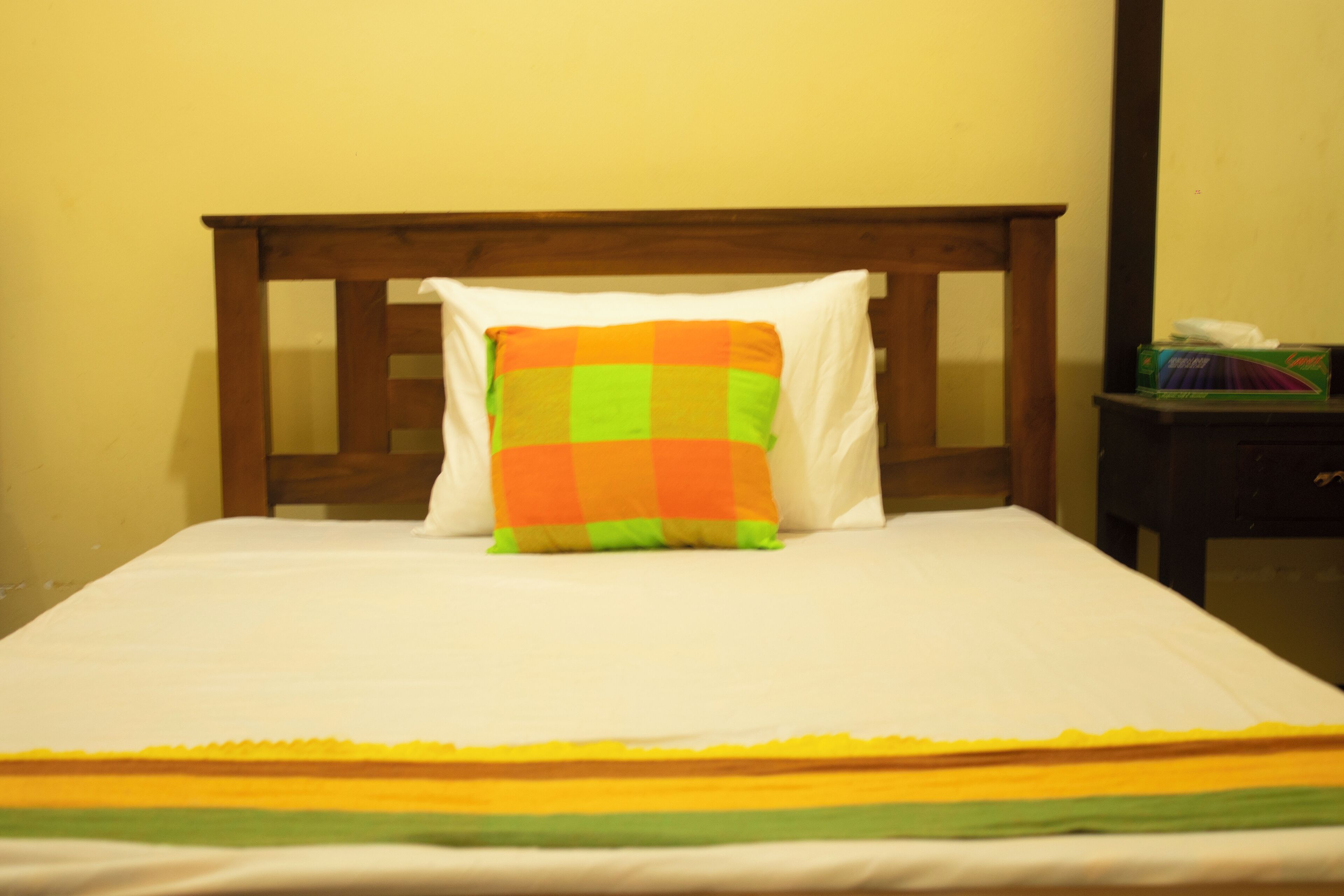 A bed with a wooden headboard, a colorful pillow, and a white bedsheet.