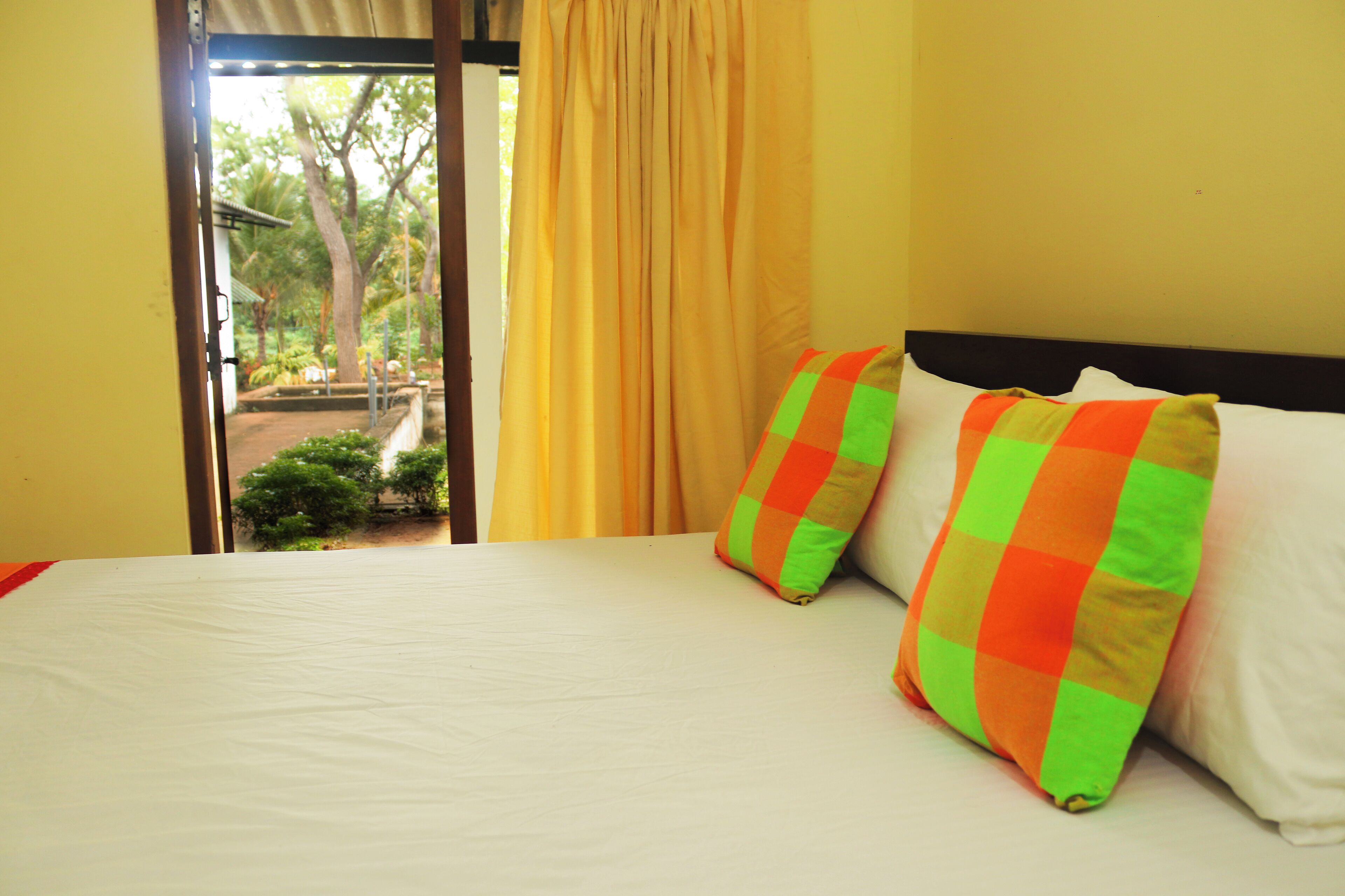 A room with a bed, two pillows, a window with curtains, and a view of greenery outside.
