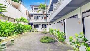 A courtyard with a paved walkway, potted plants, and a building with multiple balconies and windows. - Collection O at Jalan Padma near Legian Beach (Legian)