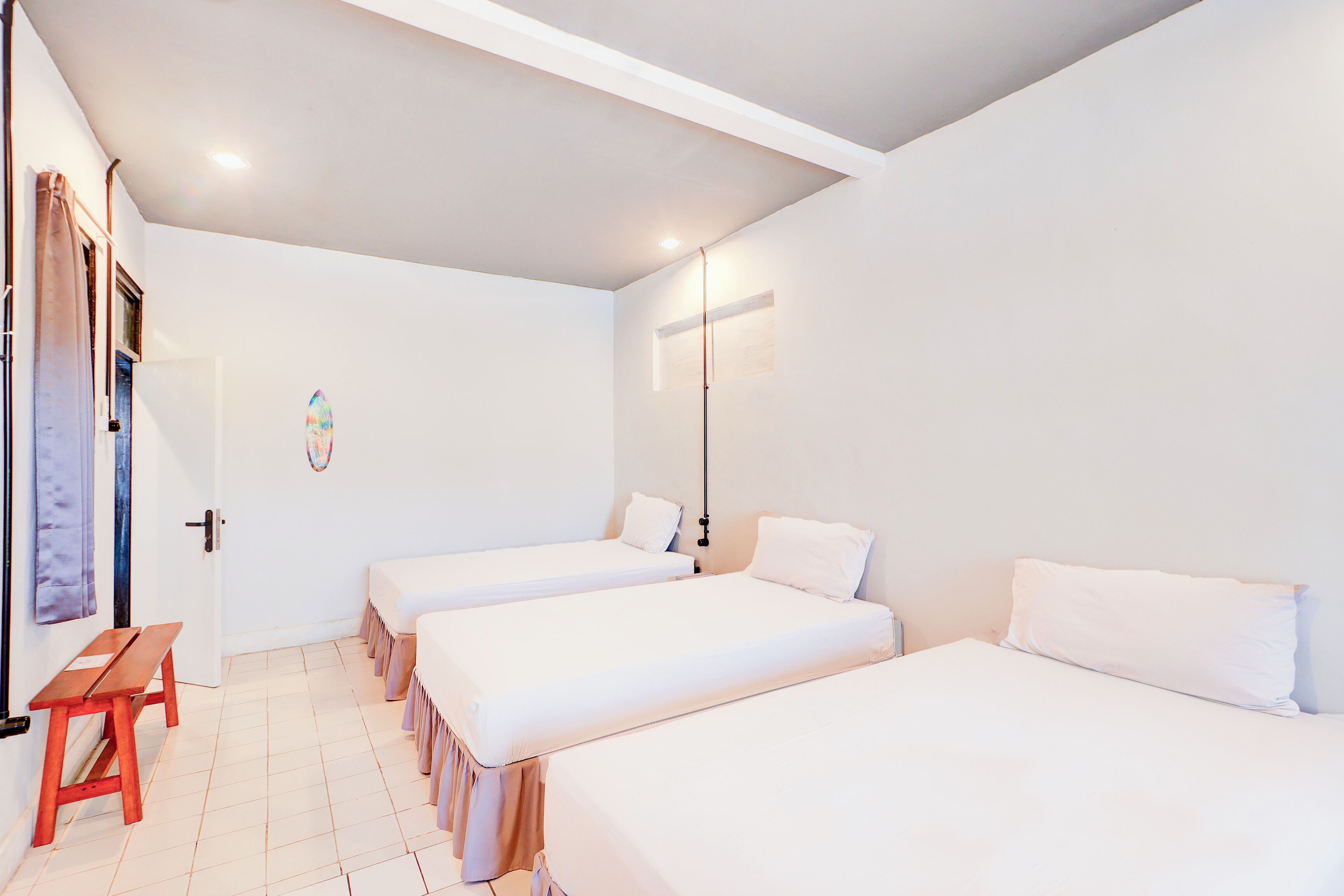 A room with three single beds, a wooden bench, and a door with a curtain.