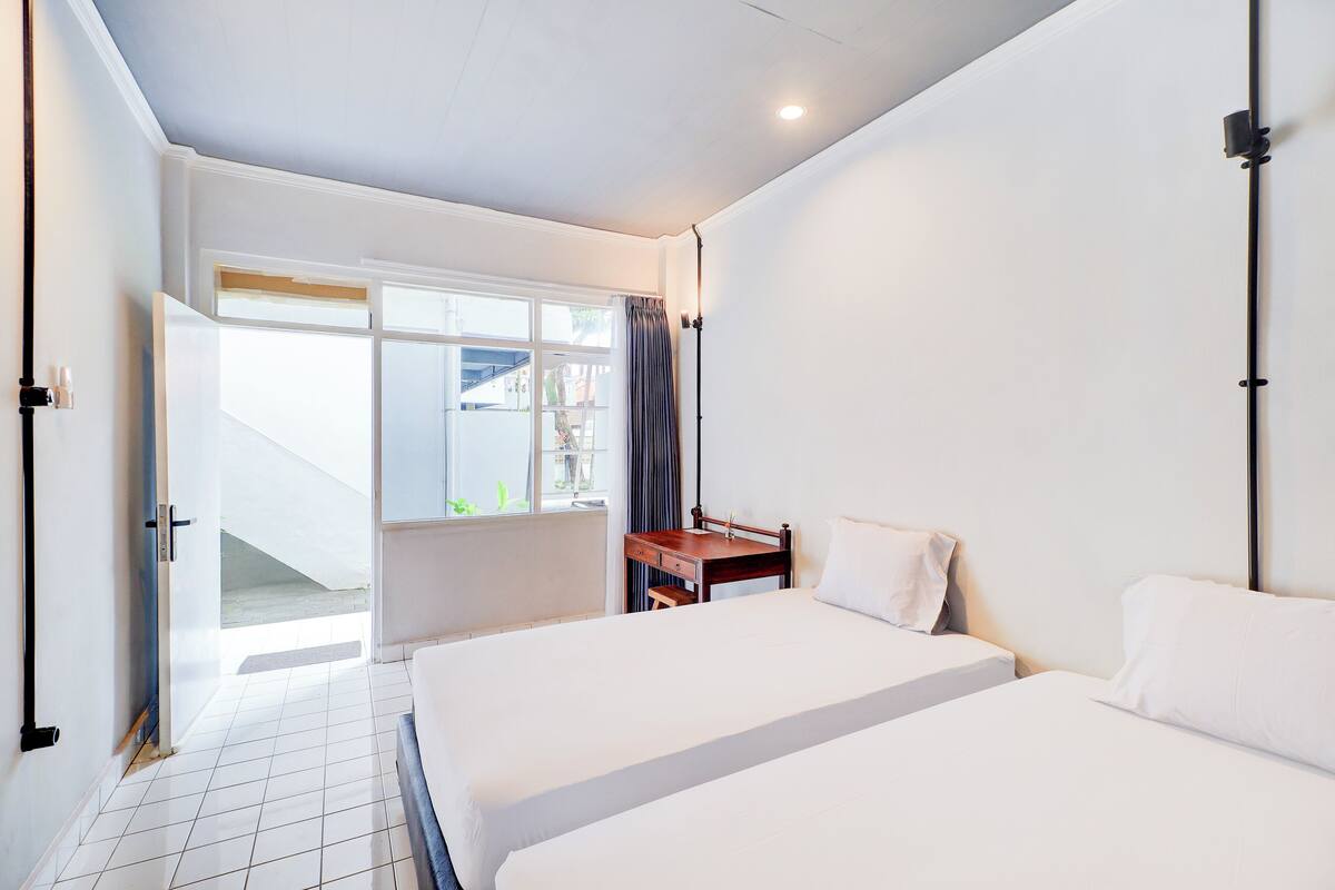 A hotel room with two beds, a desk, and a window with curtains.