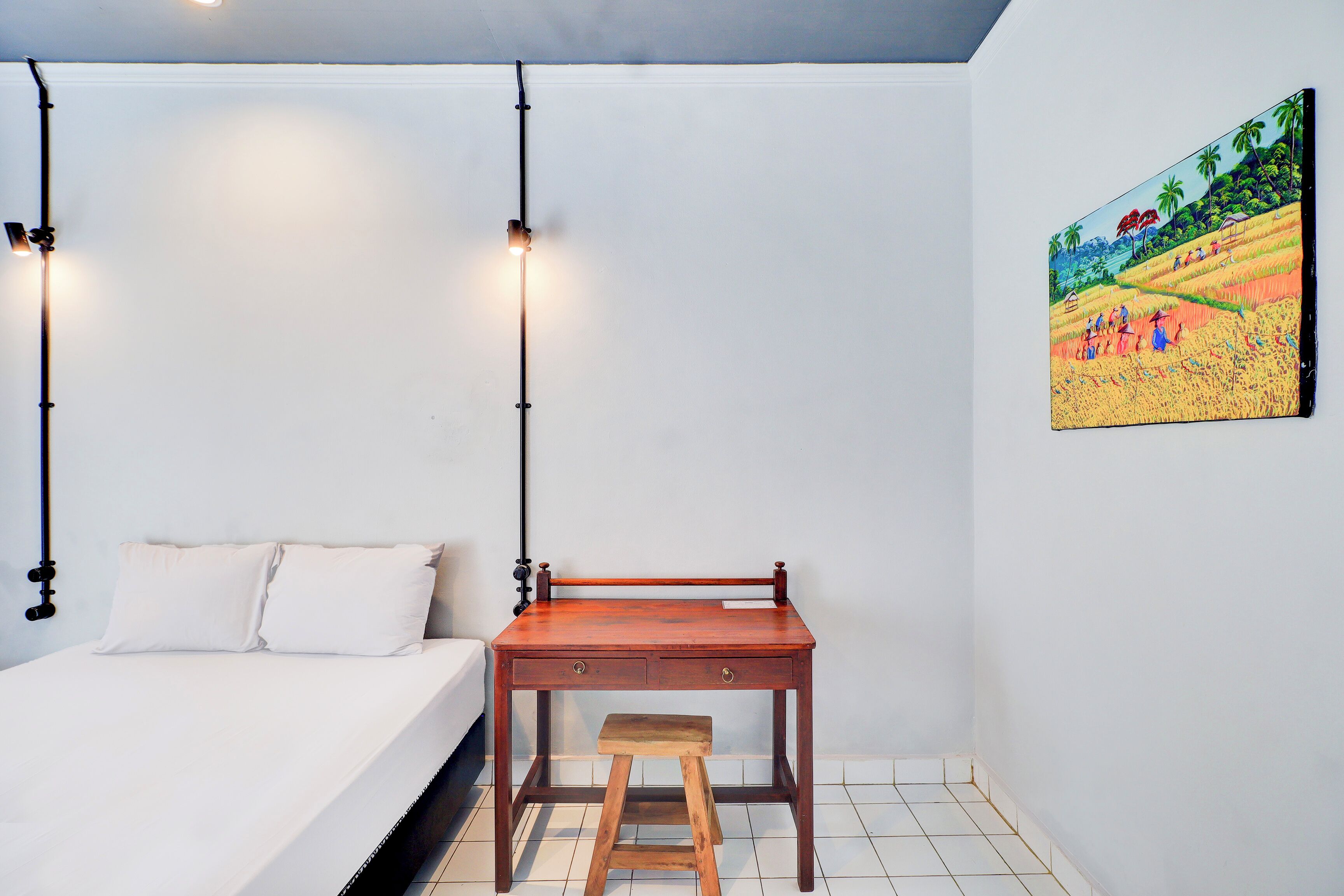 Un dormitorio con una cama, un escritorio de madera, un taburete y un cuadro en la pared.