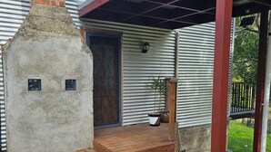 Un bâtiment doté d’une cheminée en briques, d’une porte en métal avec une poignée décorative, d’un porche en bois avec des marches et d’un mur en métal ondulé.
