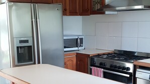 Une cuisine dotée de meubles en bois, d’un réfrigérateur en acier inoxydable, d’un four à micro-ondes, d’une cuisinière et d’un four encastré.