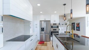 A modern kitchen with white cabinets, stainless steel appliances, and pendant lighting.