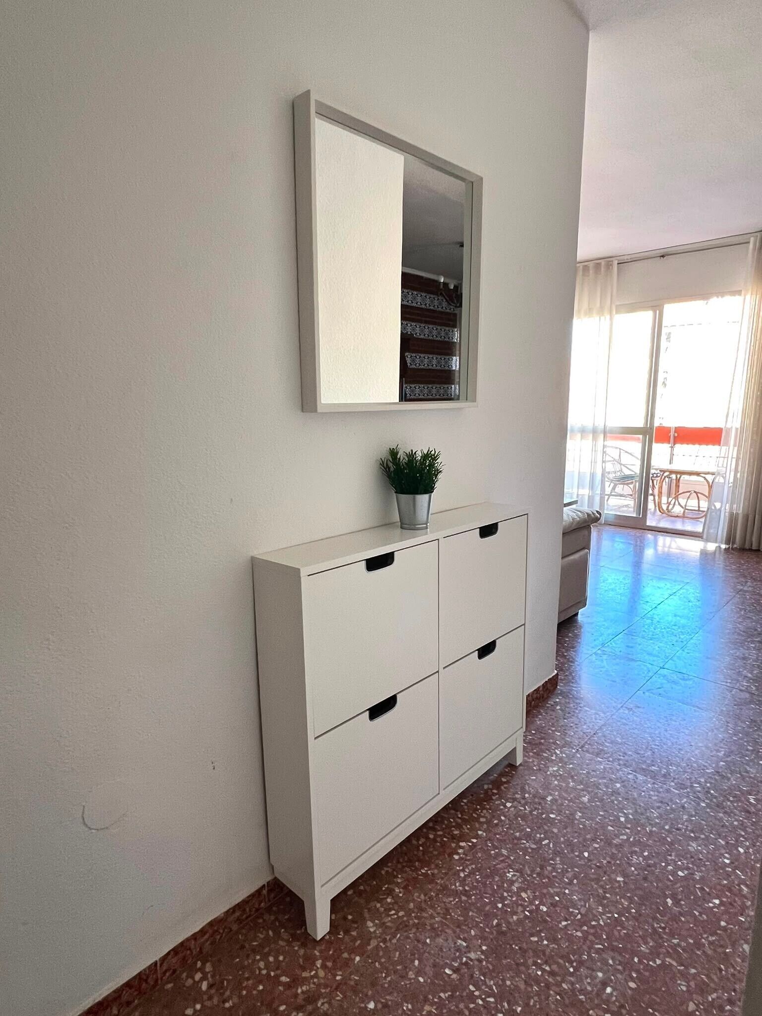 Un mueble blanco con cajones, una planta en maceta encima y un espejo arriba.