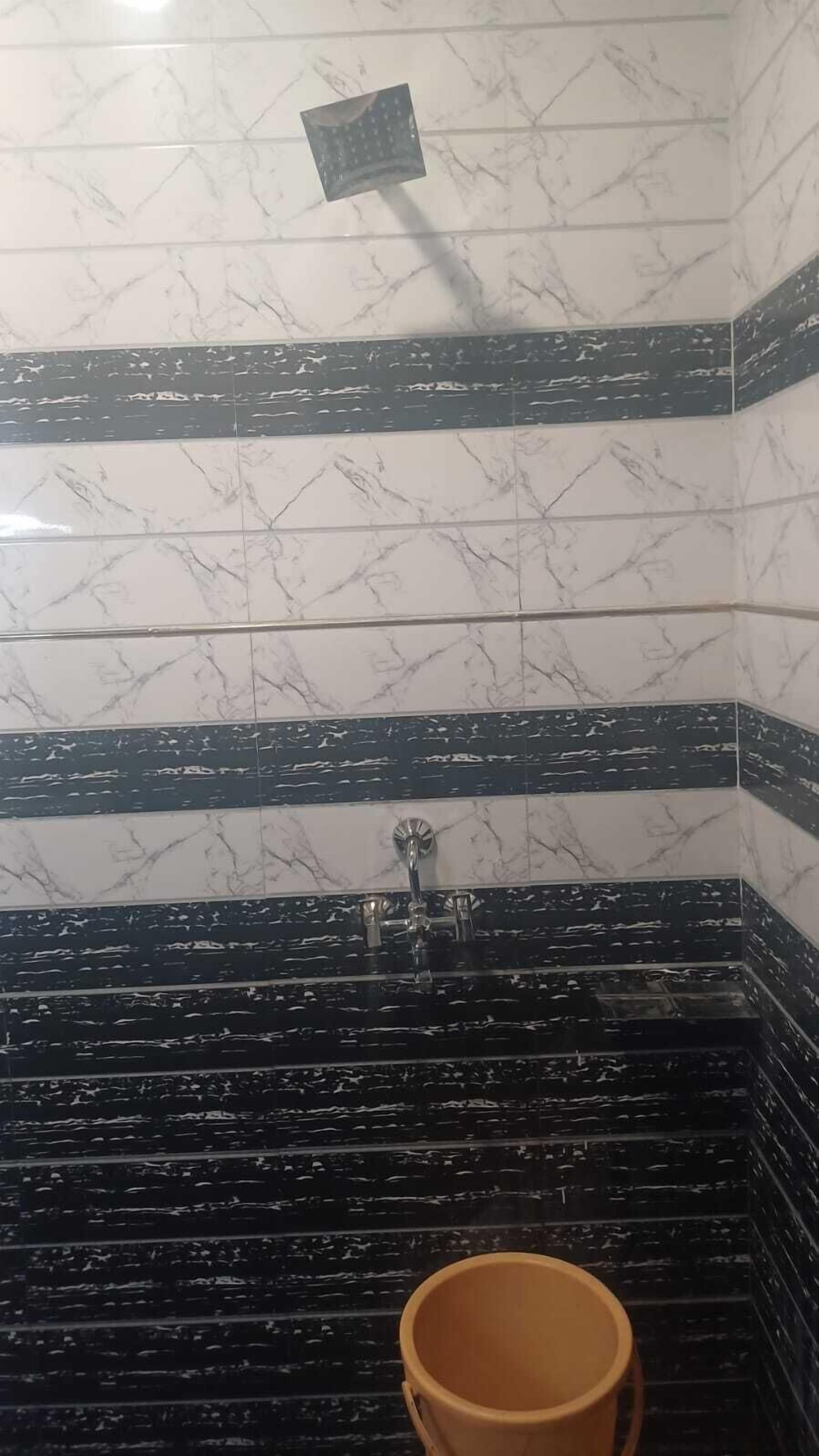 A bathroom with white marble tiles and black accents, a shower area, and a yellow bucket.
