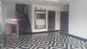 Un couloir doté d’un sol à motifs géométriques, un escalier et un espace d’accueil avec un comptoir et des plantes.