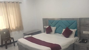 Une chambre à coucher comprenant un lit, une table de chevet, une chaise, un appareil de climatisation et une fenêtre avec des rideaux.