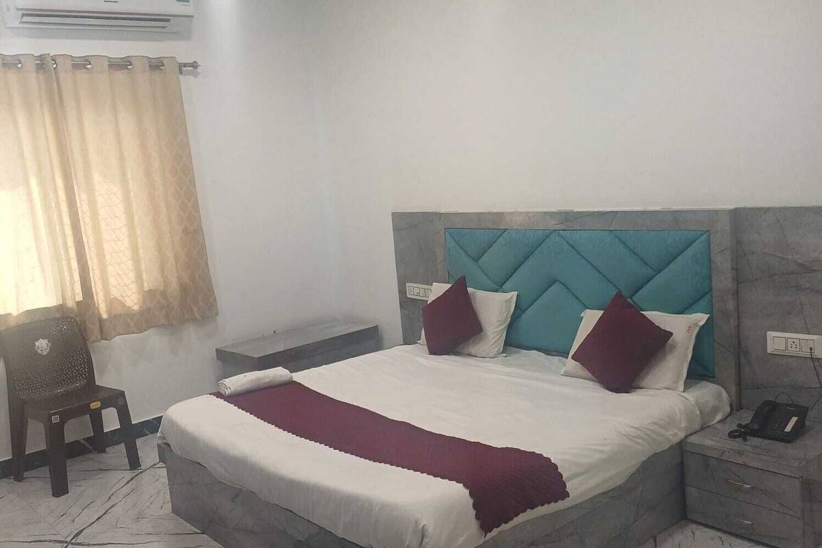 Une chambre à coucher comprenant un lit, une table de chevet, une chaise, un appareil de climatisation et une fenêtre avec des rideaux.