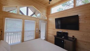Ein Schlafzimmer mit Holzwänden, einem Bett, einem an der Wand montierten Fernseher und einem Fenster mit Jalousien.