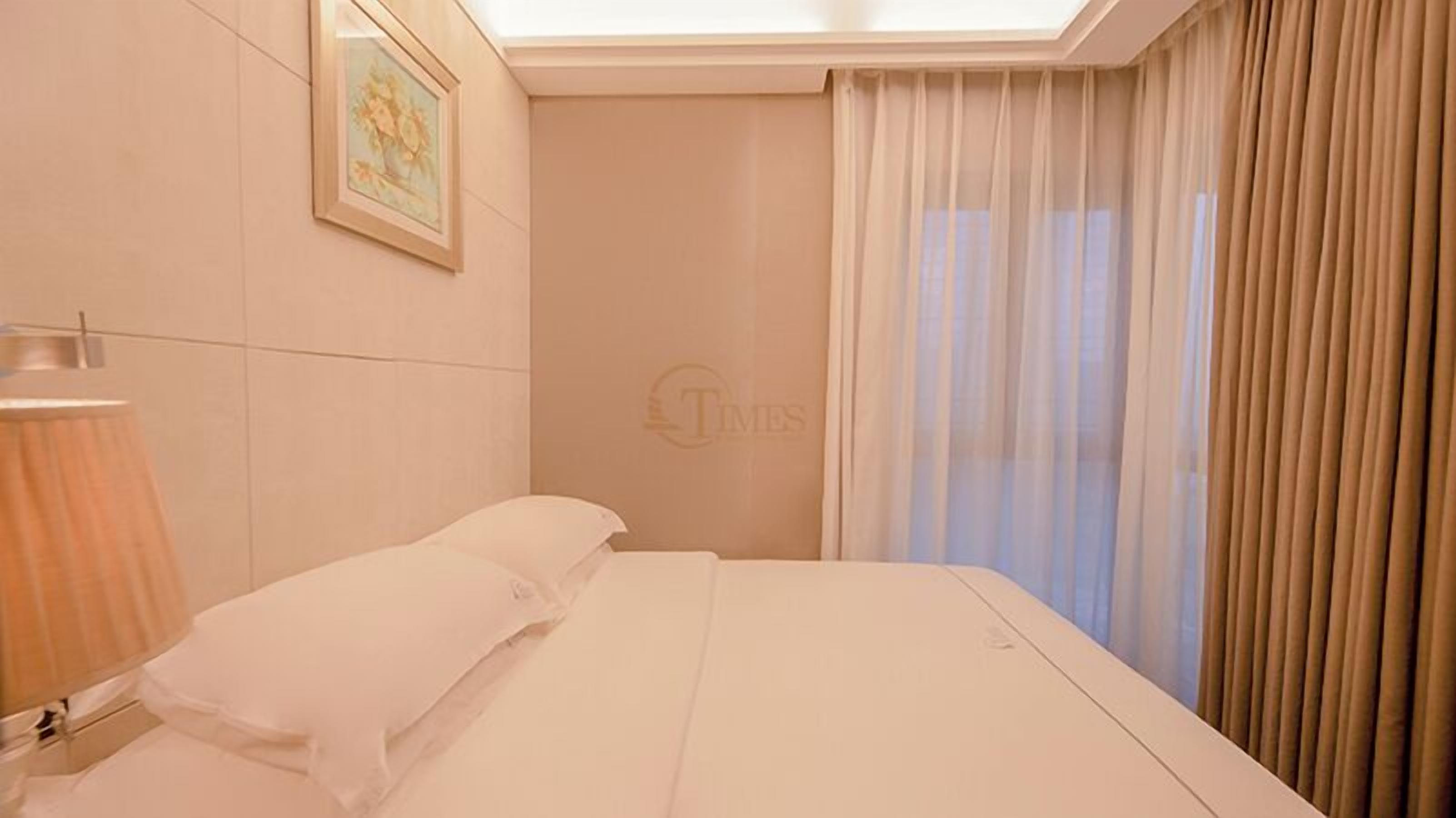Une chambre d’hôtel avec un lit, une table de chevet, une lampe et une fenêtre avec des rideaux.