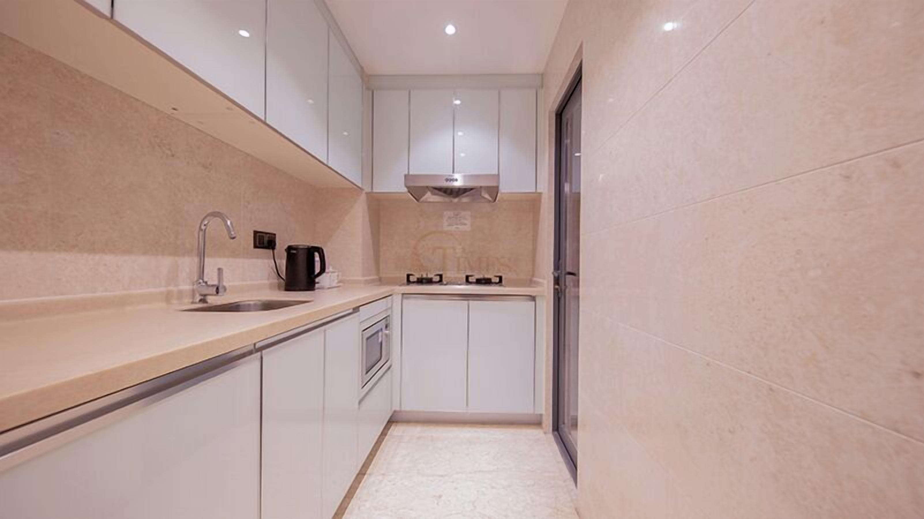 A compact kitchen with white cabinets, a stainless steel sink, a black kettle, and a built-in stove.
