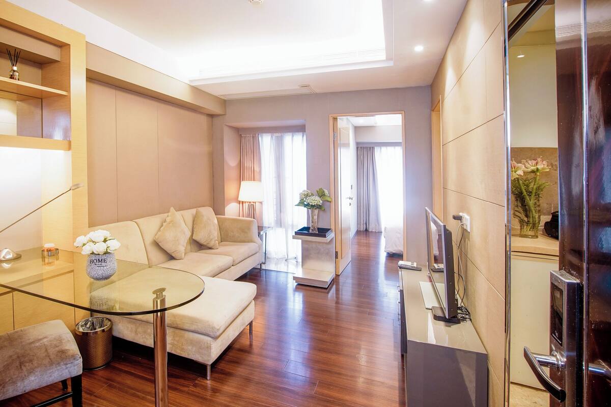 Una habitación de hotel moderna con una mesa de comedor de vidrio, un sofá, un televisor y un pasillo que lleva a otra habitación.