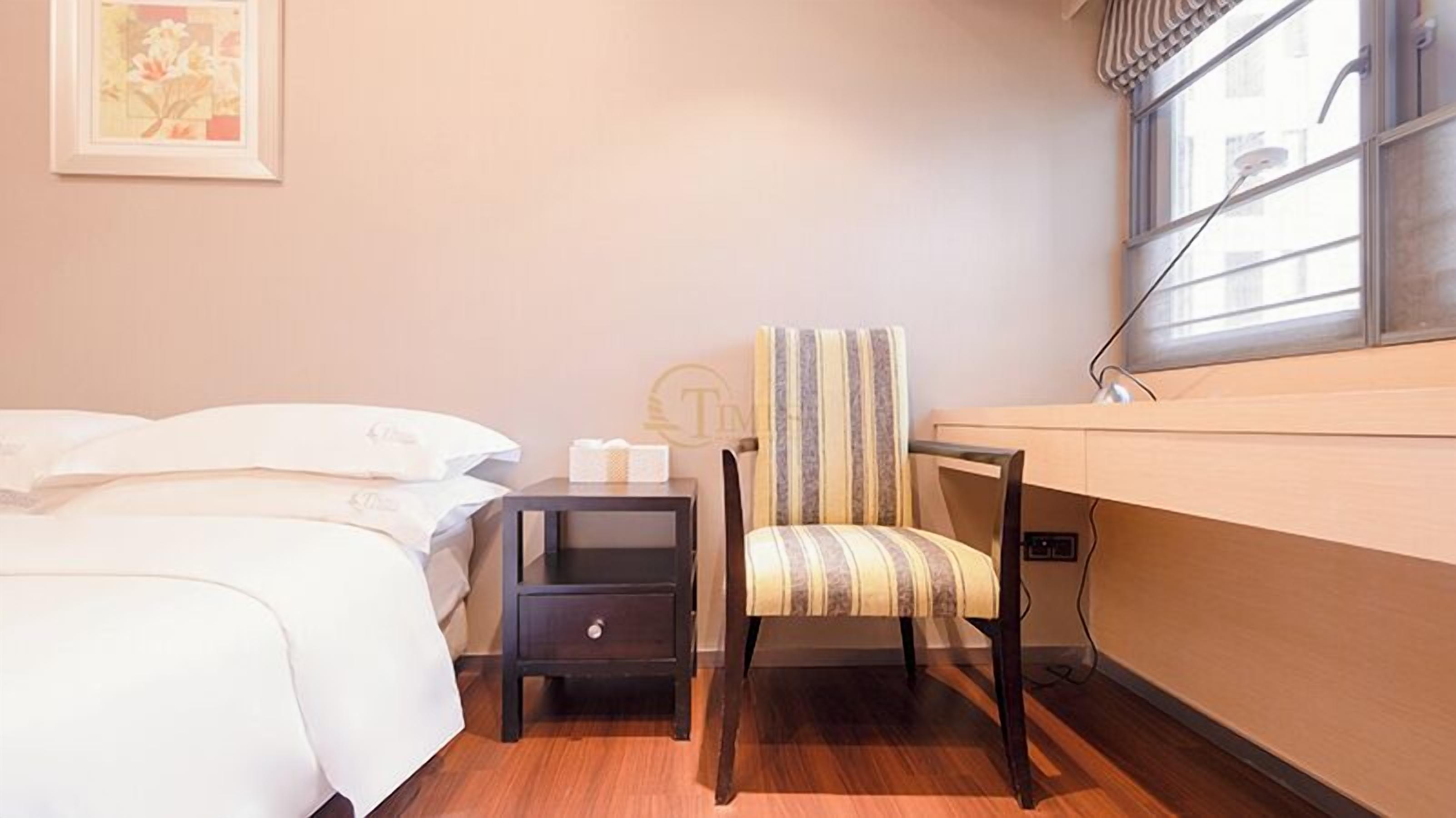 A bedroom with a bed, a nightstand, a chair, and a window with a shower.