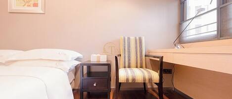 A bedroom with a bed, a nightstand, a chair, and a window with a shower.