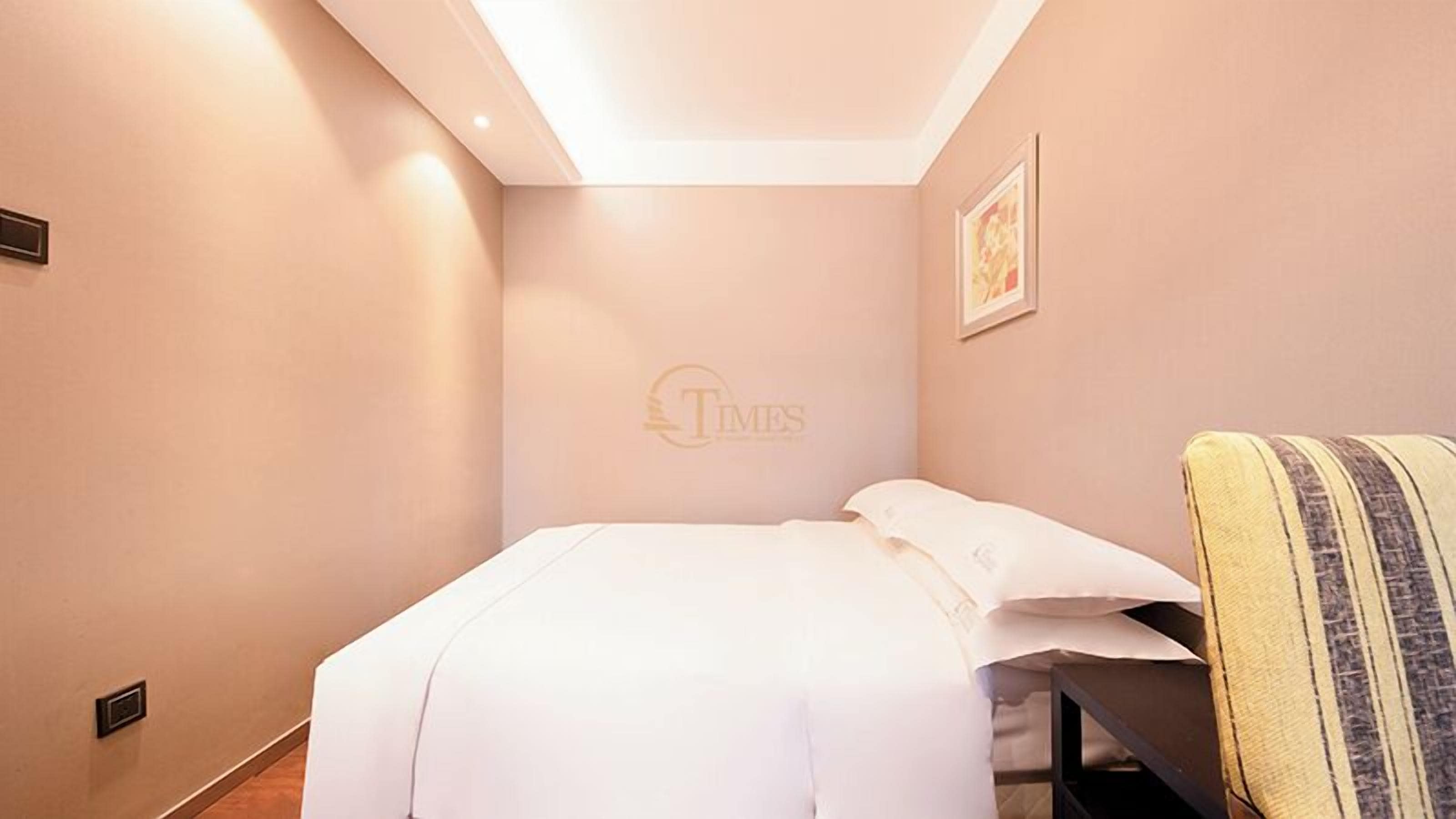 A hotel room with a neatly made bed, a small bedside table, and a framed picture on the wall.