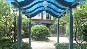 A covered walkway with a blue roof and spherical lights, surrounded by lush greenery and a building in the background. - Tianxi Apartment KKone Branch (Shenzhen)