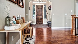 A hallway with a wooden door, a bench, a vase with branches, and a chandelier.