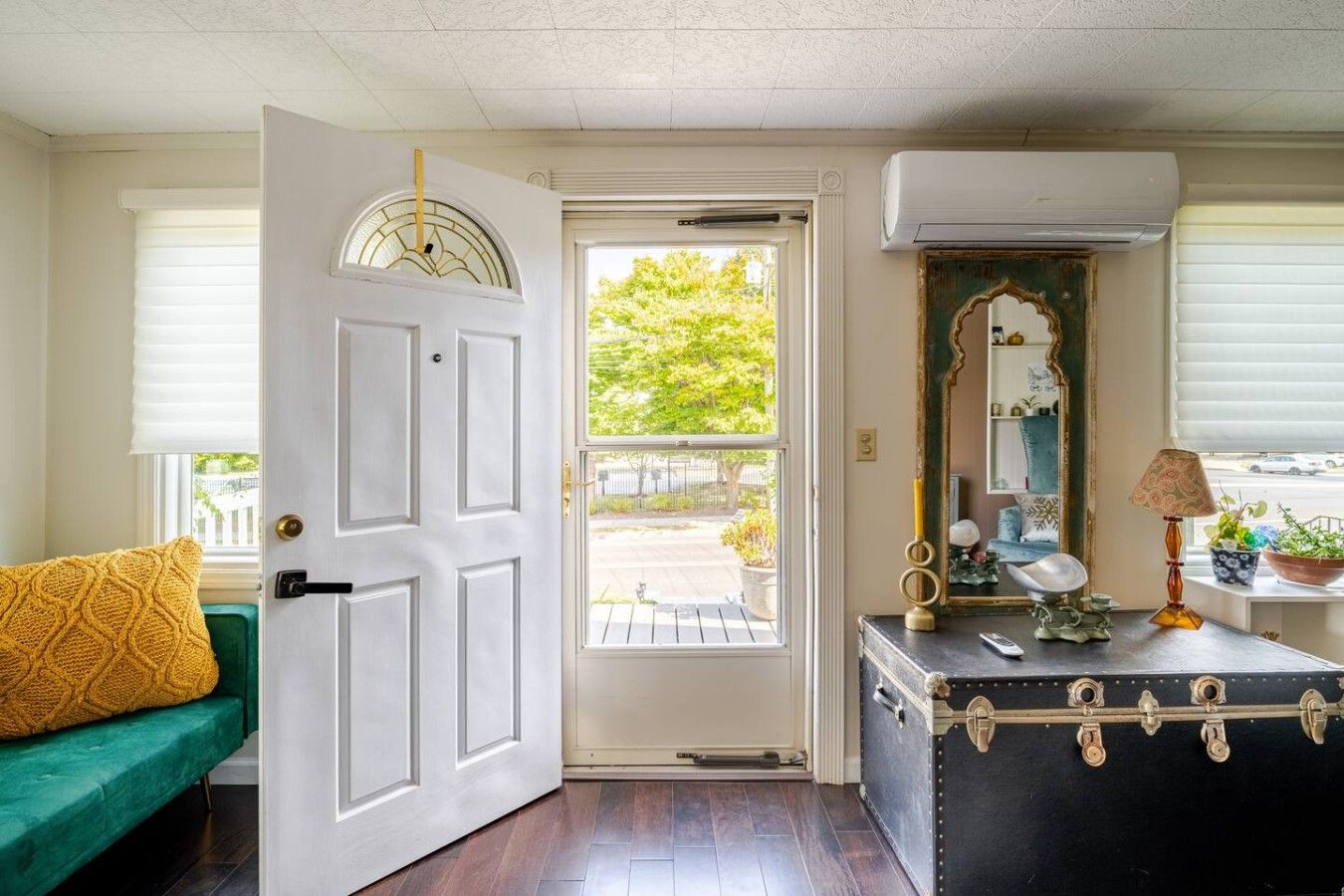 A room with a white door, a green couch, a black dresser with a mirror, and an air conditioning unit.