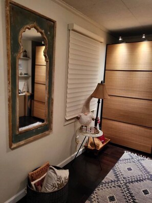 Une pièce avec un grand miroir, une lampe, une petite table ornée d’un objet décoratif et un tapis à motifs.