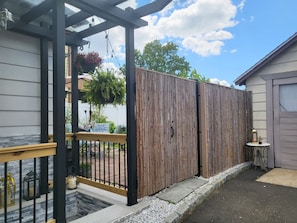 Un espace extérieur clos, délimité par une clôture en bois, une porte en métal et agrémenté d’une petite table avec une lampe.