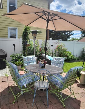 Une terrasse avec une table ronde et des chaises, un grand parasol et des plantes en pot.