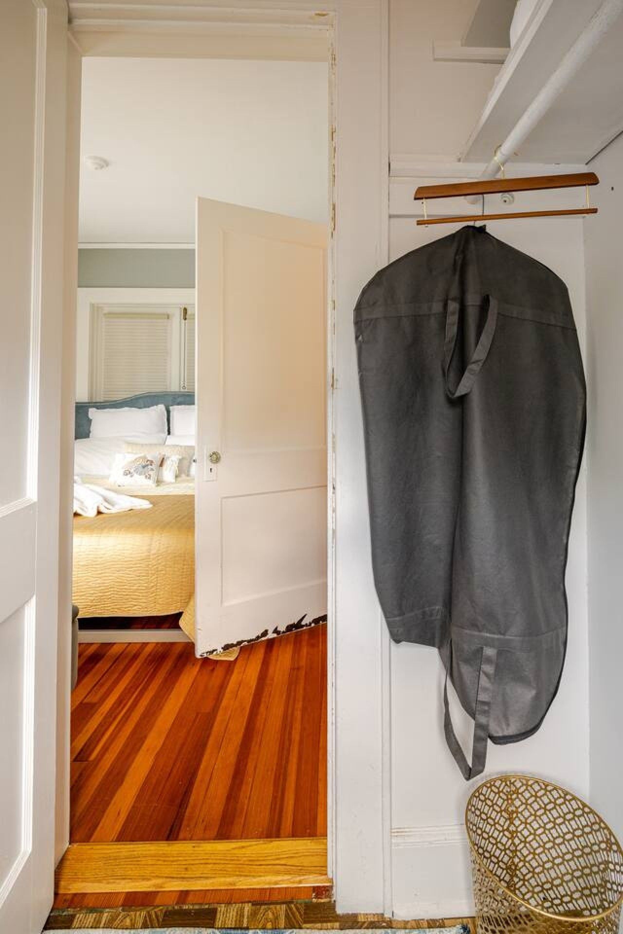 A hotel room with a wooden floor, a bed with white bedding, and a coat hanging on a rack.
