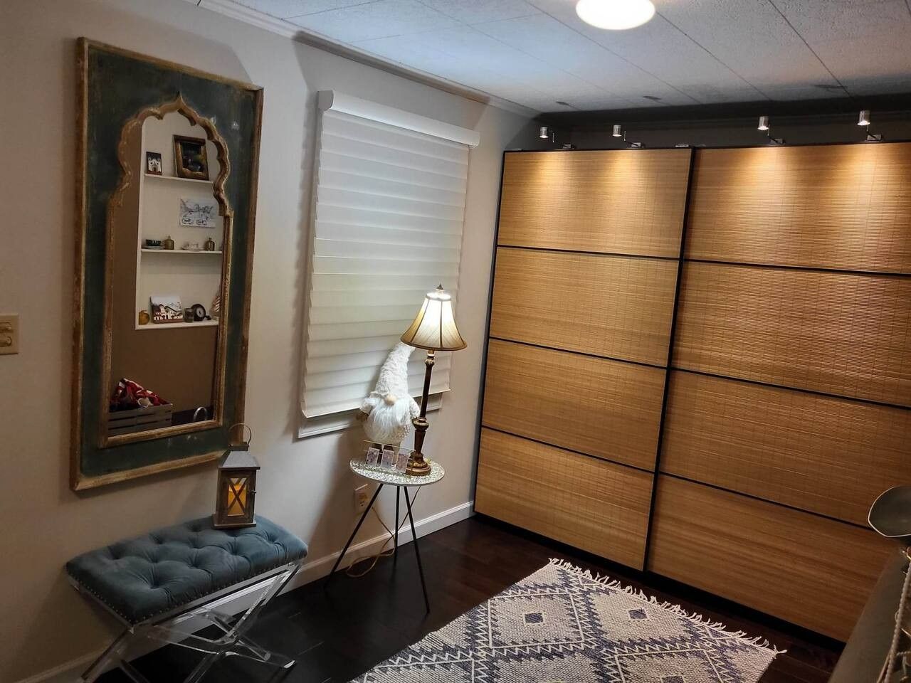Una habitación con un espejo grande, una lámpara, un banco acolchado azul y una alfombra estampada.