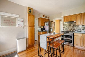 Une cuisine avec des meubles de rangement en bois, un réfrigérateur, une cuisinière et un tabouret de bar.