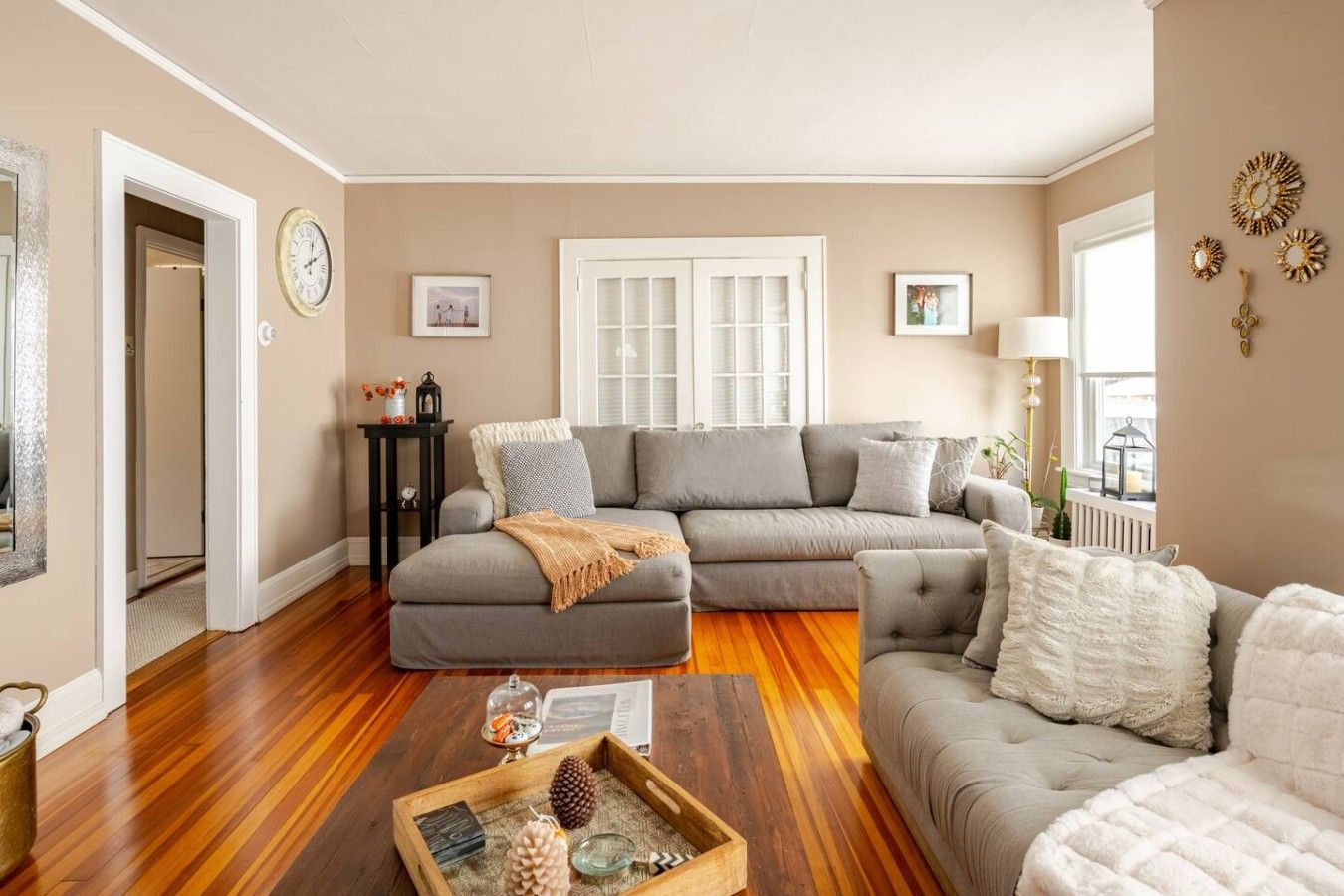 A living room with a sectional sofa, a coffee table with decorative items, a clock on the wall, and a window with blinds.